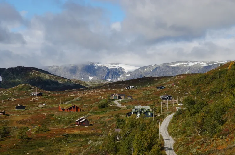 Bilde av hytter på Haugastøl i høstfarger med snøkledd fjell i bakgrunnen