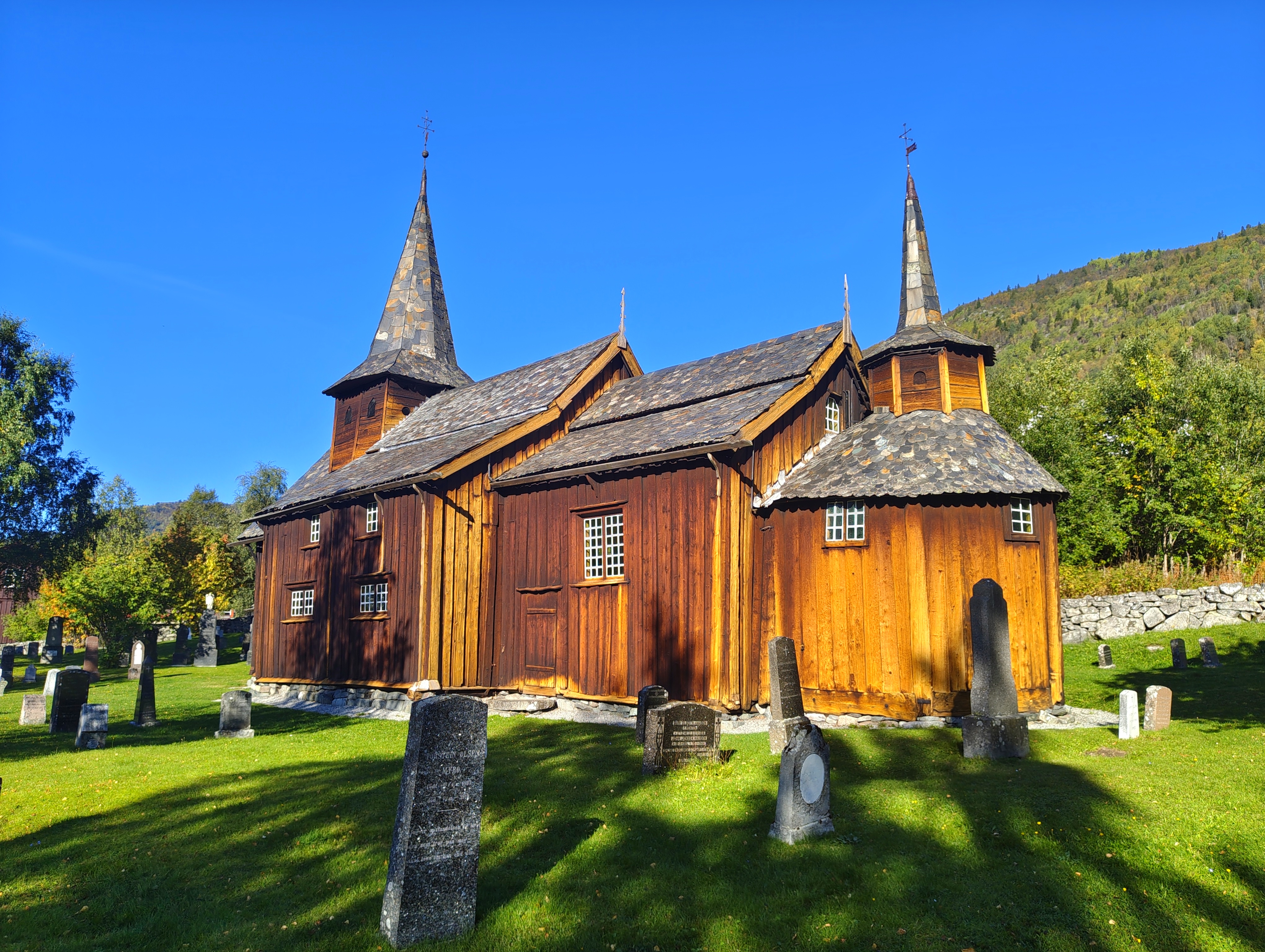 Bilde av en gammel kirke med gravsteiner rundt på en solfylt sommerdag. 