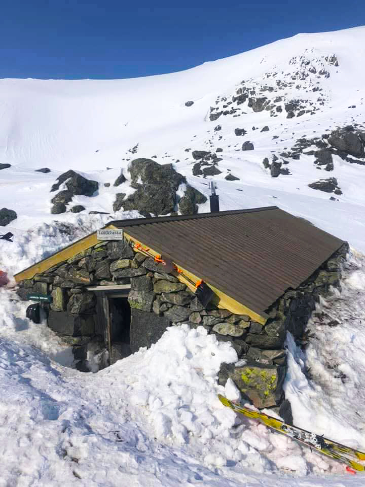 Bilde av en steinbu delvis begravd i snø i et solfylt høyfjellsområde. 