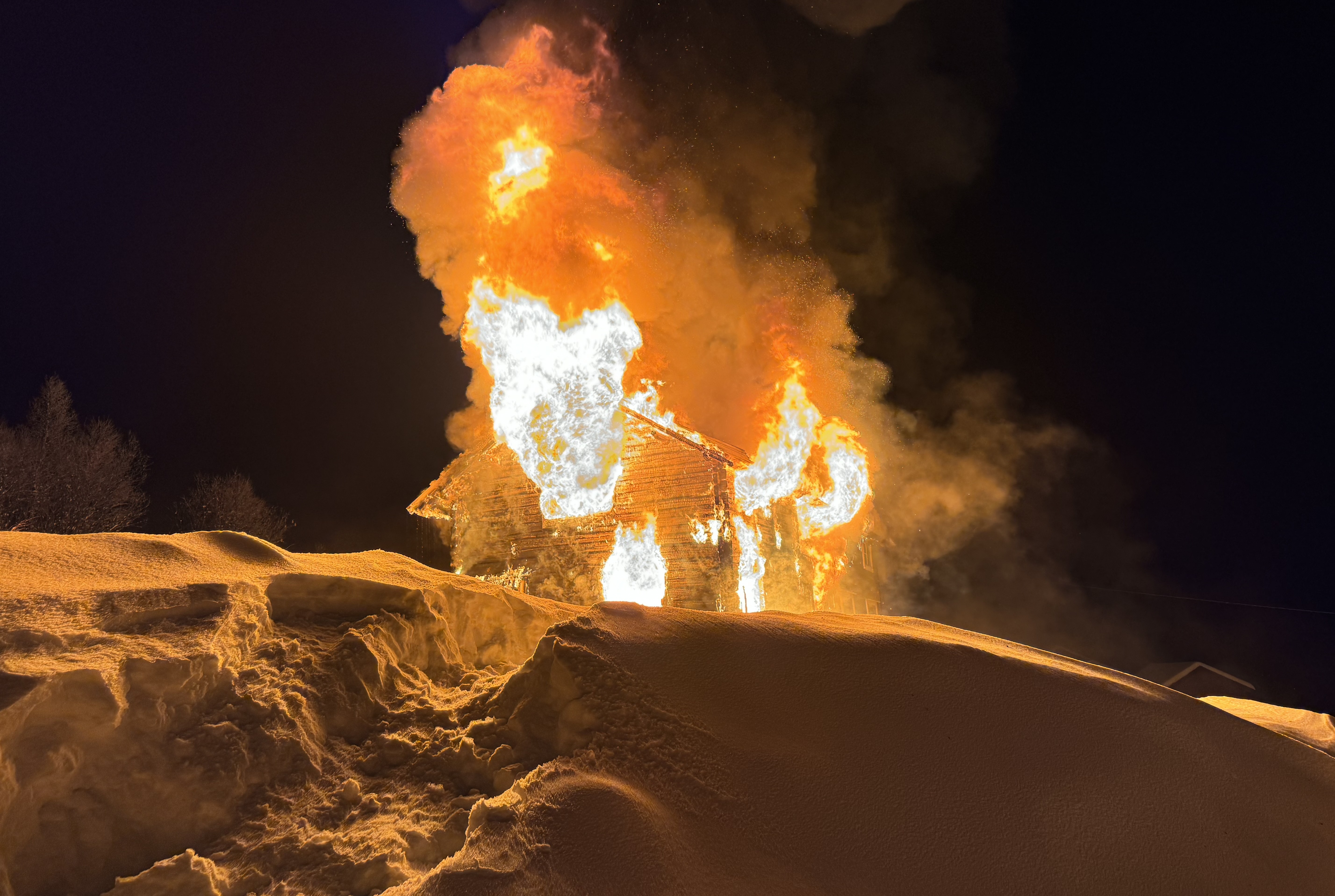 Foto av hus i brann. Flammene står ut av vinduer og tak, og lyser opp snøen rundt.