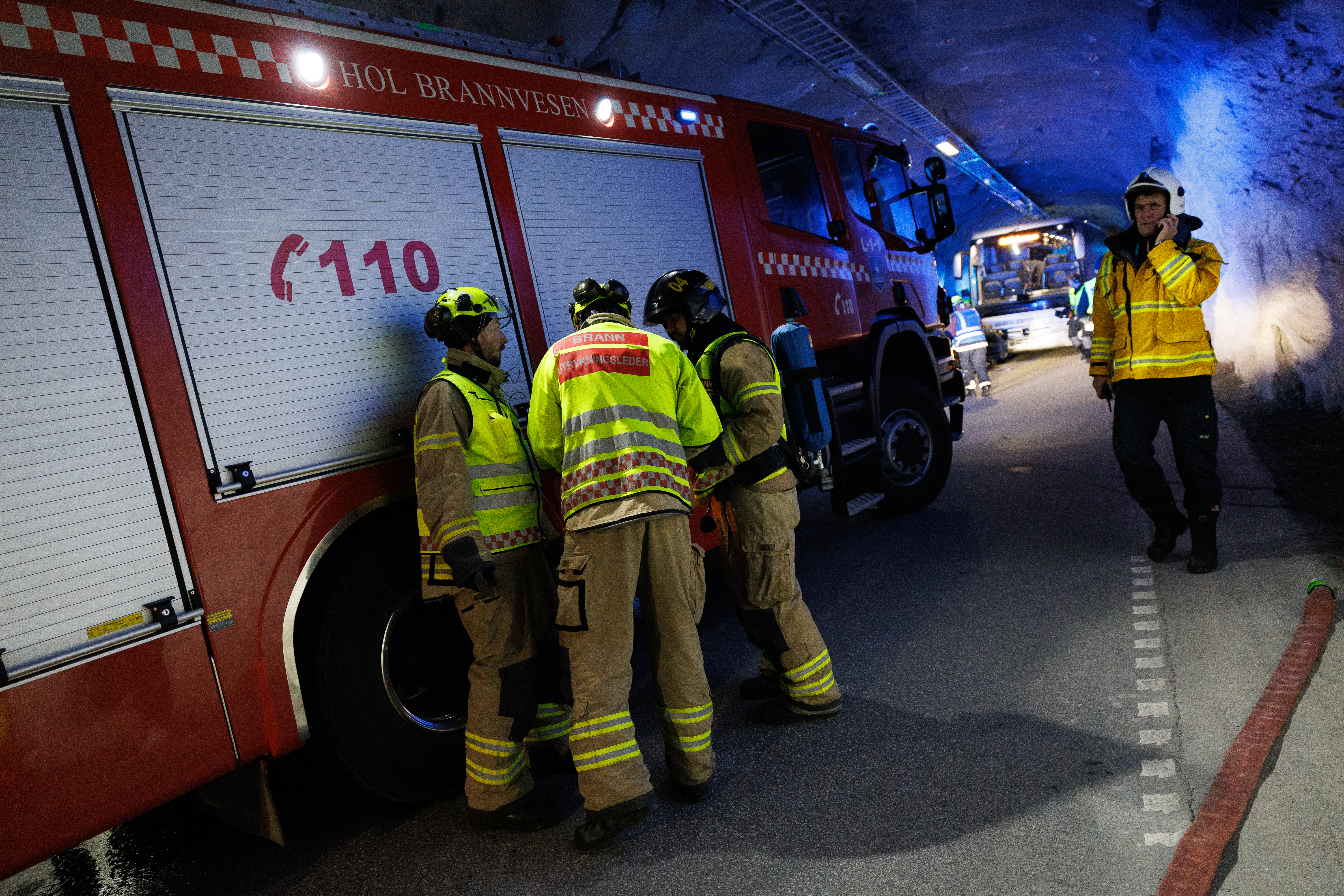 Foto av brannbil og flere brannkonstabler i uniform i en dukel tunnel.
